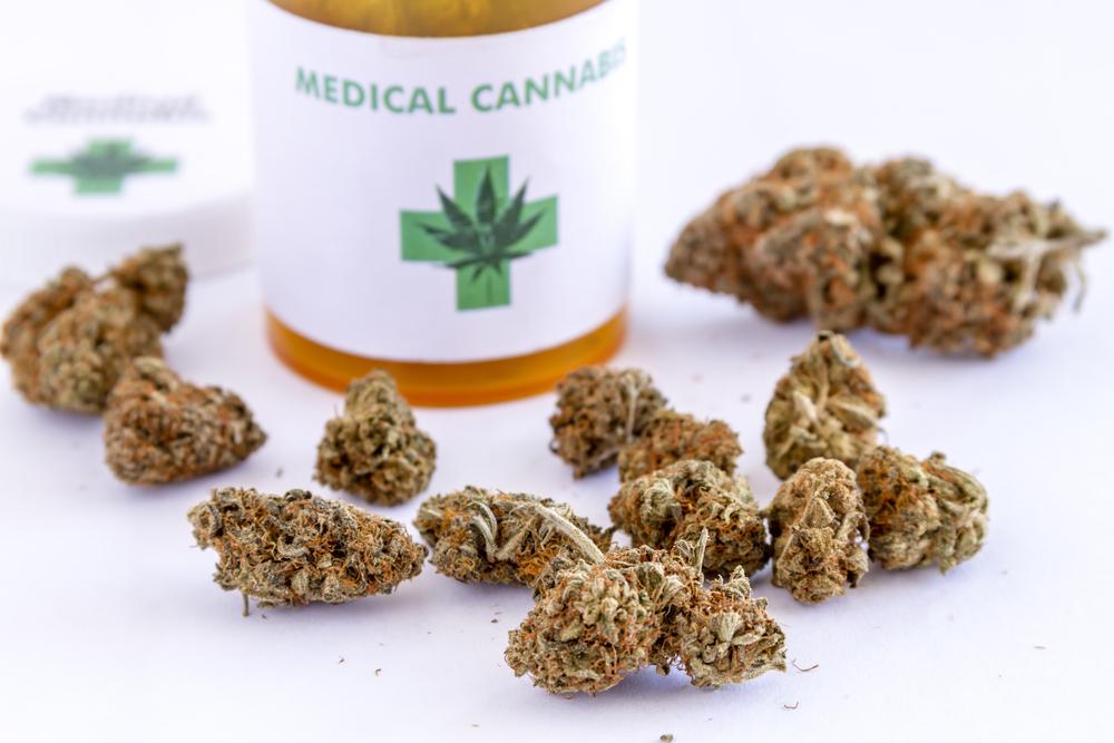 Medical marijuana buds sitting on white table top next to medical cannabis prescription bottle with lid