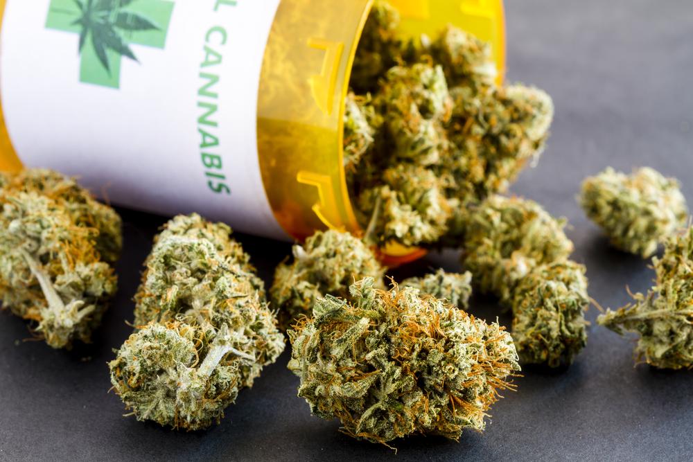 Close up of medical marijuana buds spilling out of prescription bottle with label on black background
